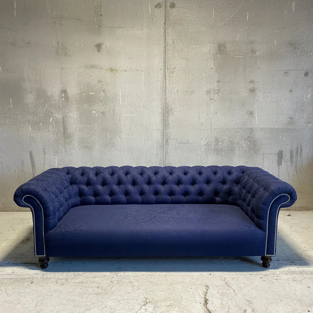 Navy blue tufted sofa in front of a large abstract painting on a white brick wall.